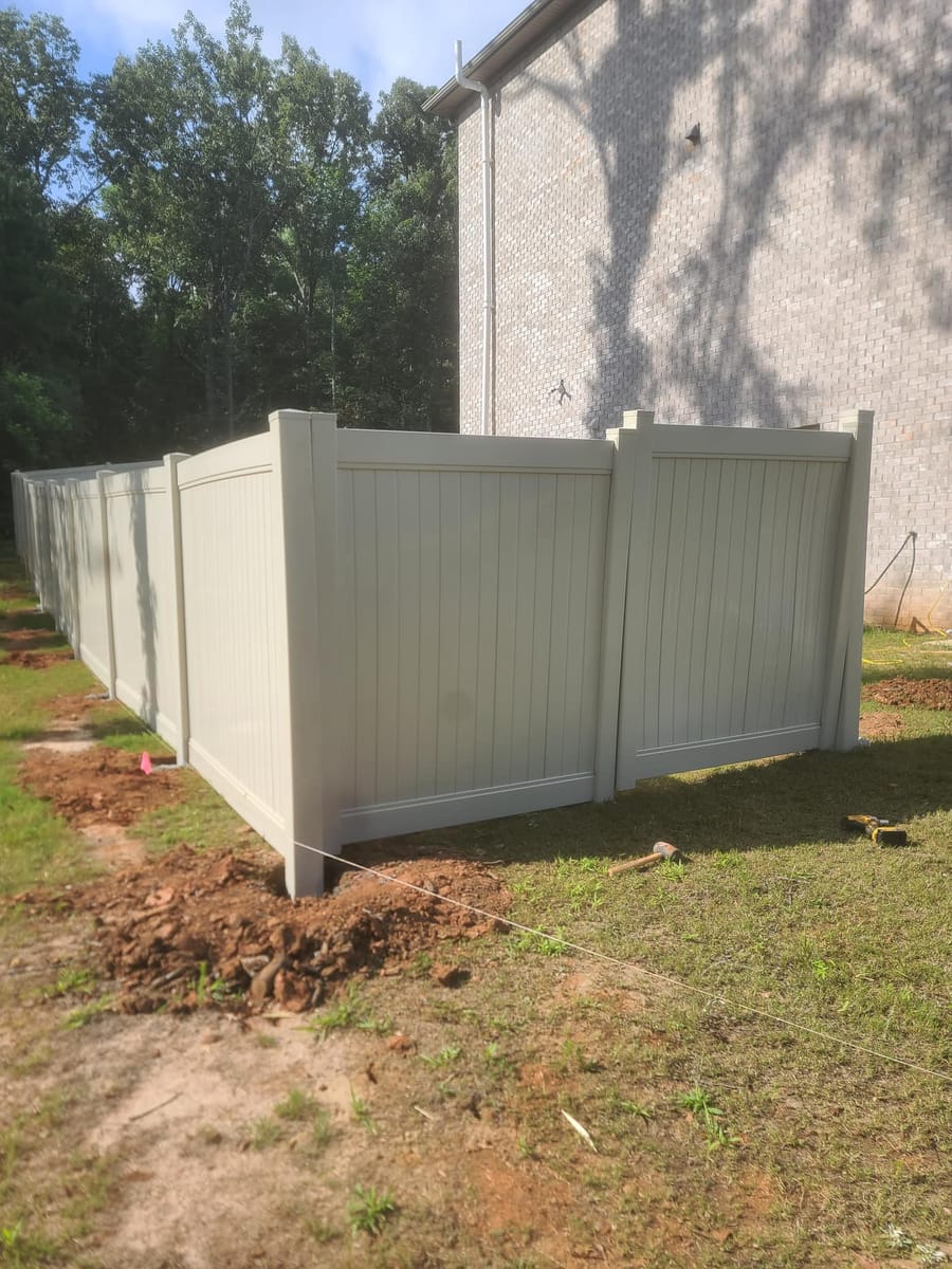 Tan vinyl privacy fence installed across a wooded residential boundary, Stockbridge, Georgia
